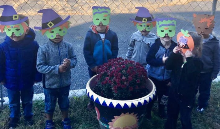 Children in costumes standing around a potted plant