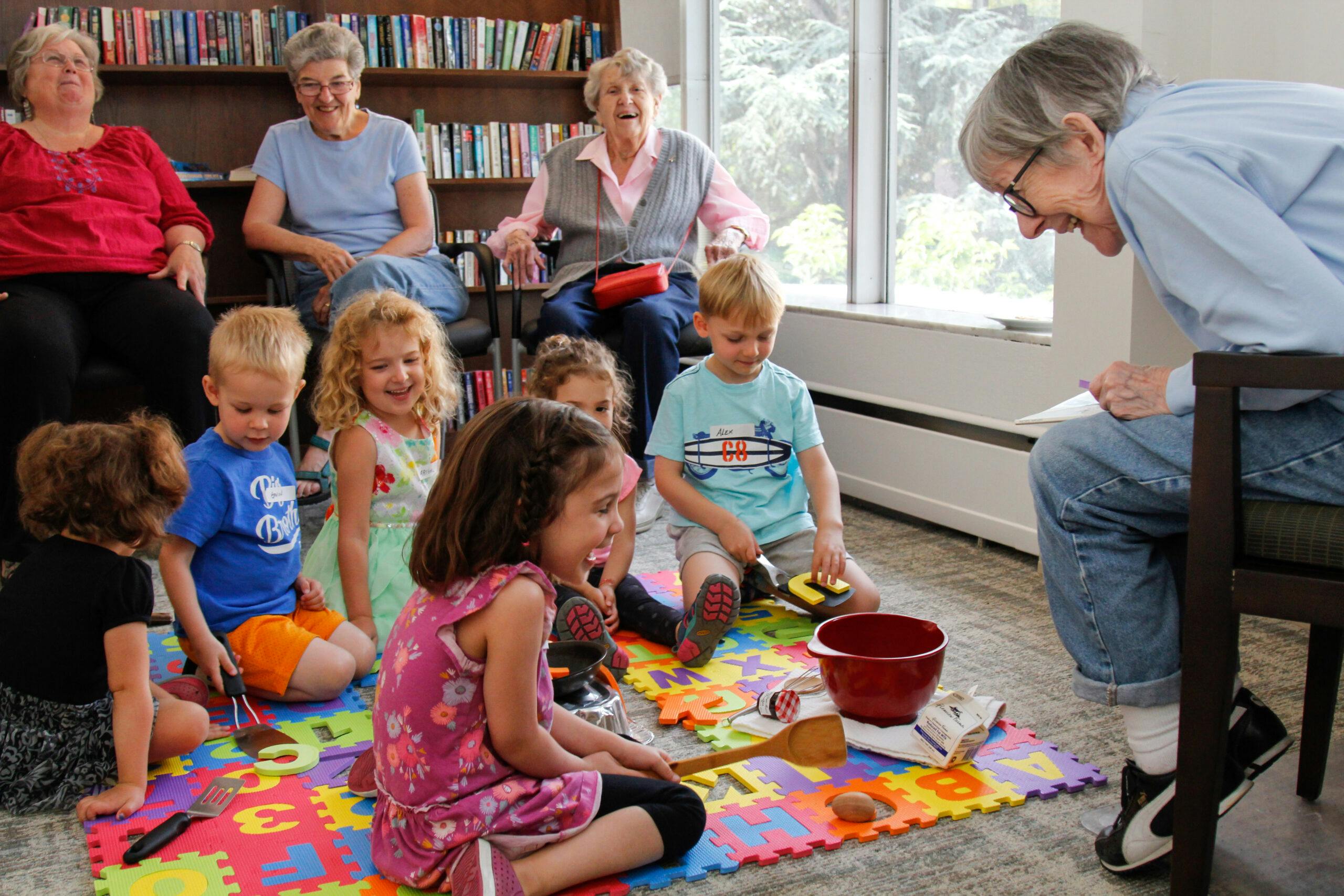 Children playing with toy food on colorful mats while adults watch