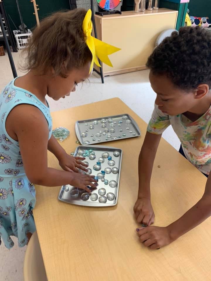 Two children playing with glass beads on trays at a table