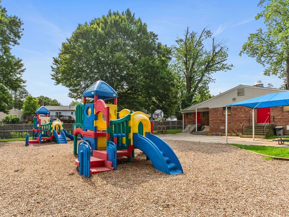 Colorful playground set with slides on wood chips, next to a brick building