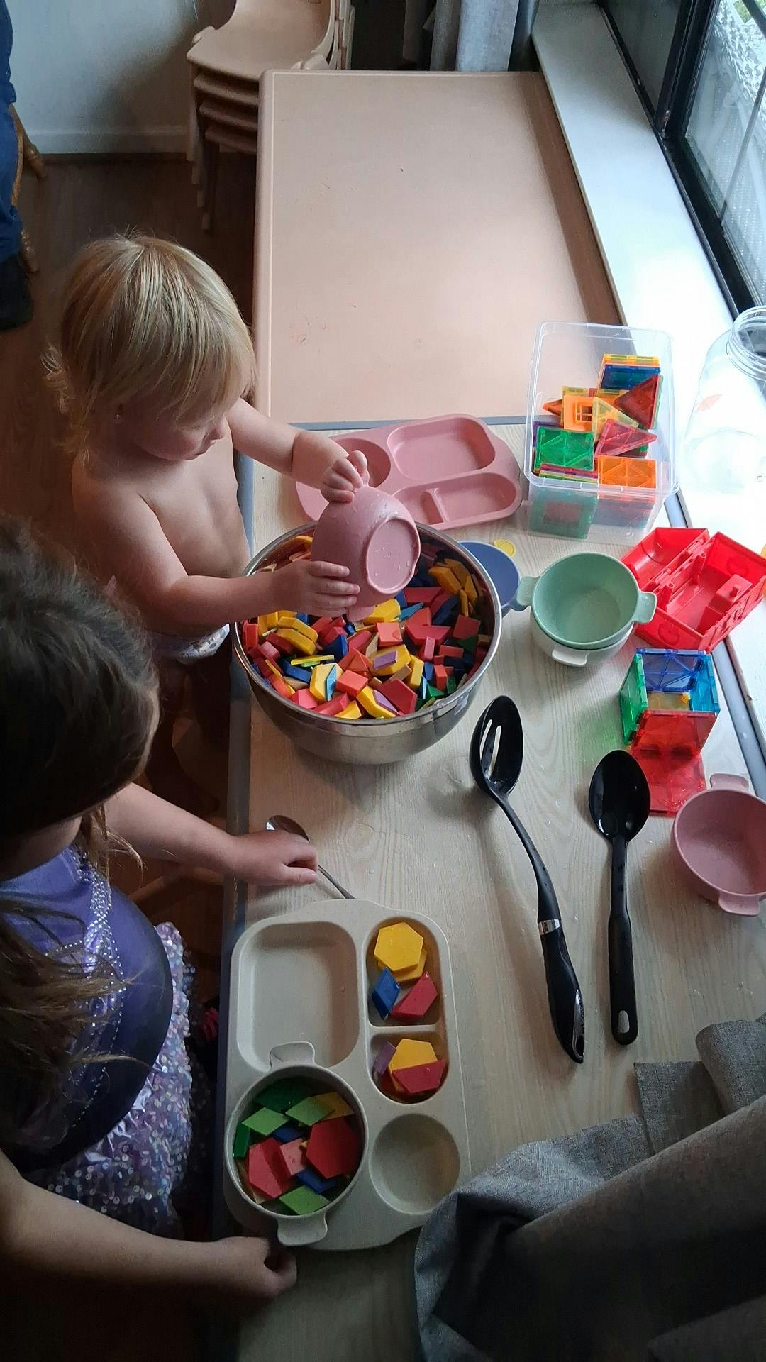 Child pouring block shapes from a bowl into a metal pot, mixing bowl, bowl