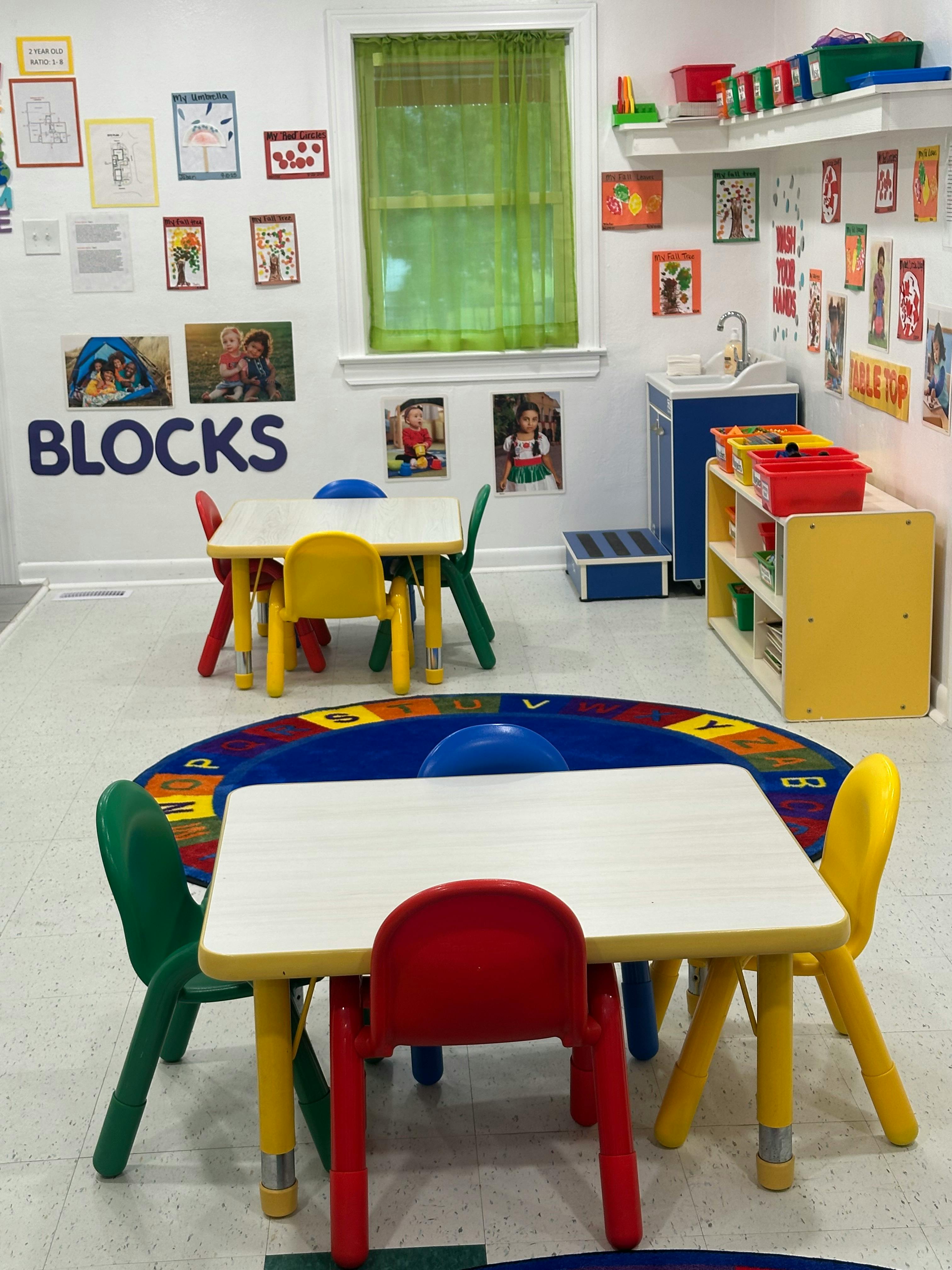 Classroom with small tables and chairs, a rug, and wall decorations