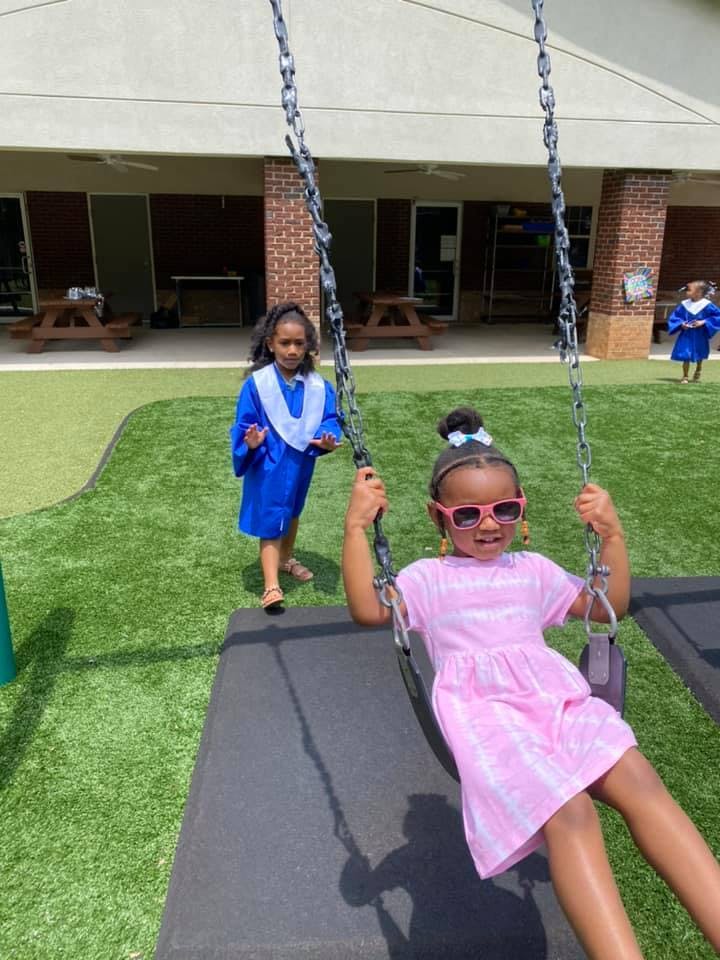 Child in pink dress on a swing, another child in blue behind