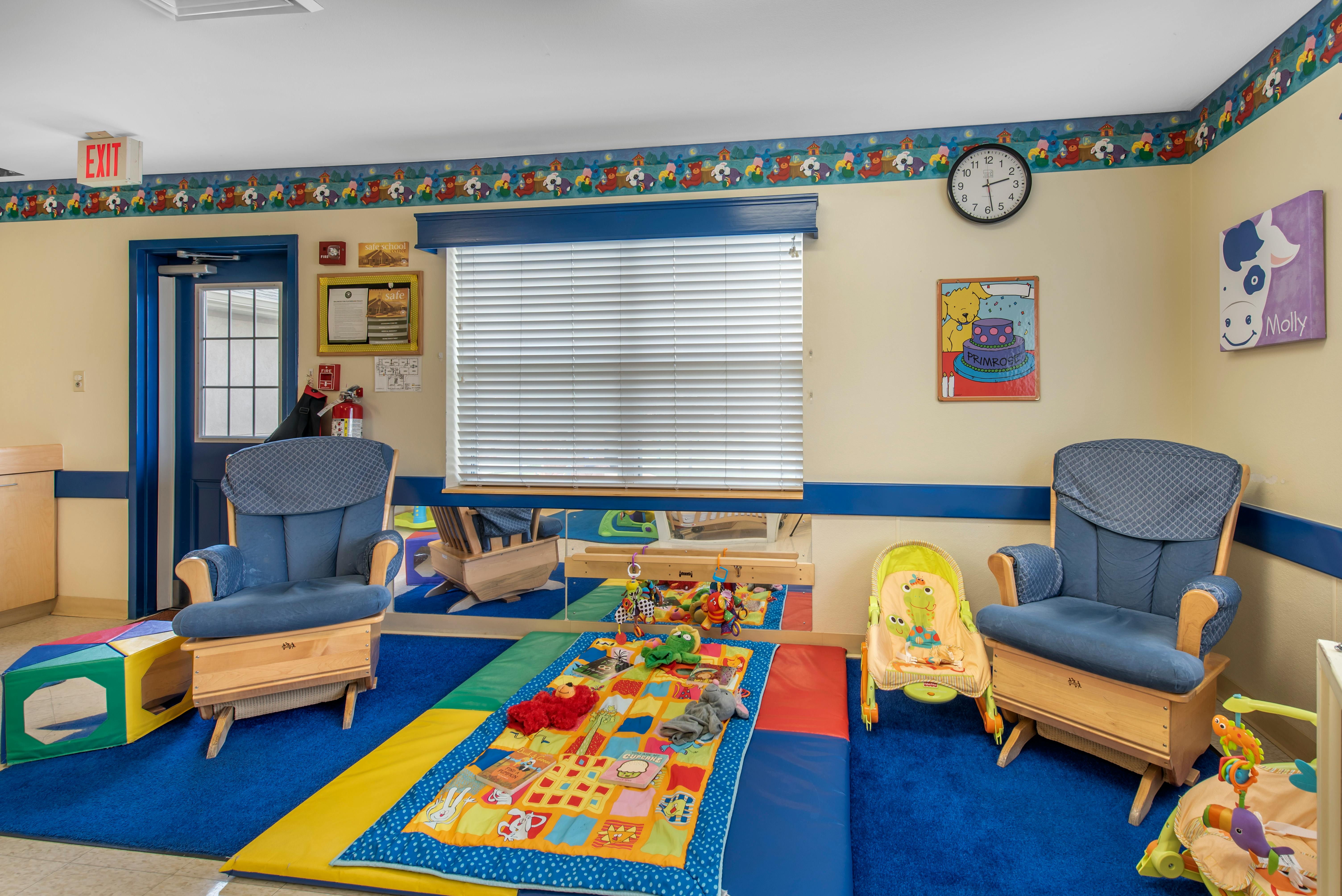 Baby classroom with chairs, a playmat with toys, and an exit sign