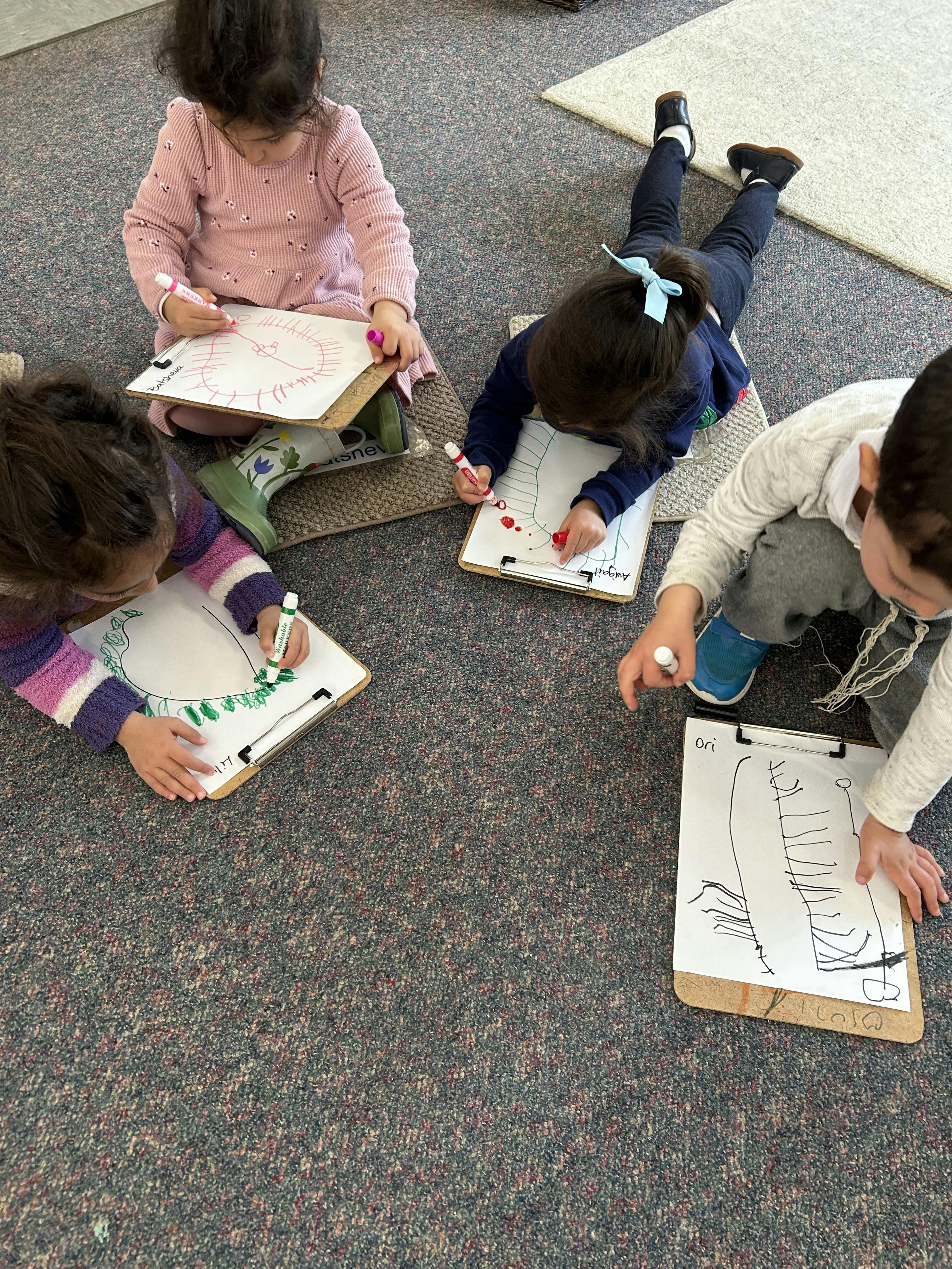 Four children lying on the floor drawing on clipboards