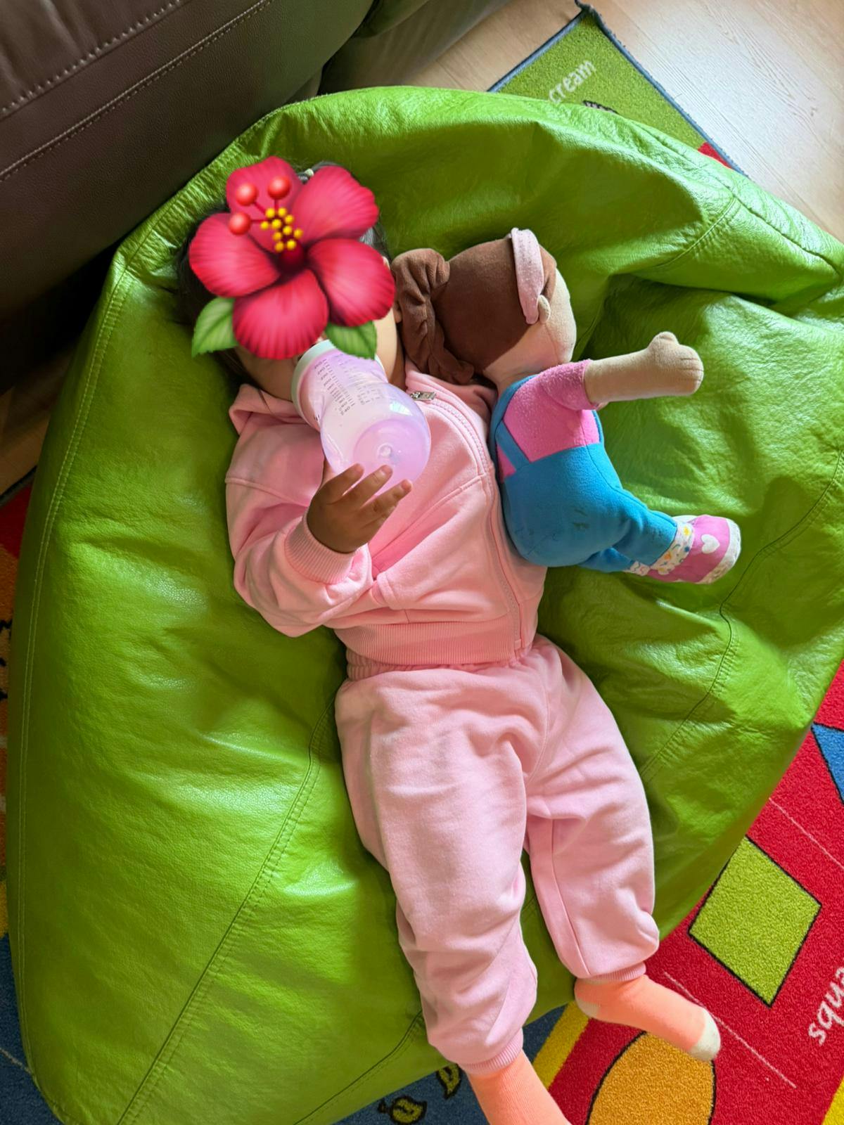Child lying on a beanbag chair holding a bottle and a doll