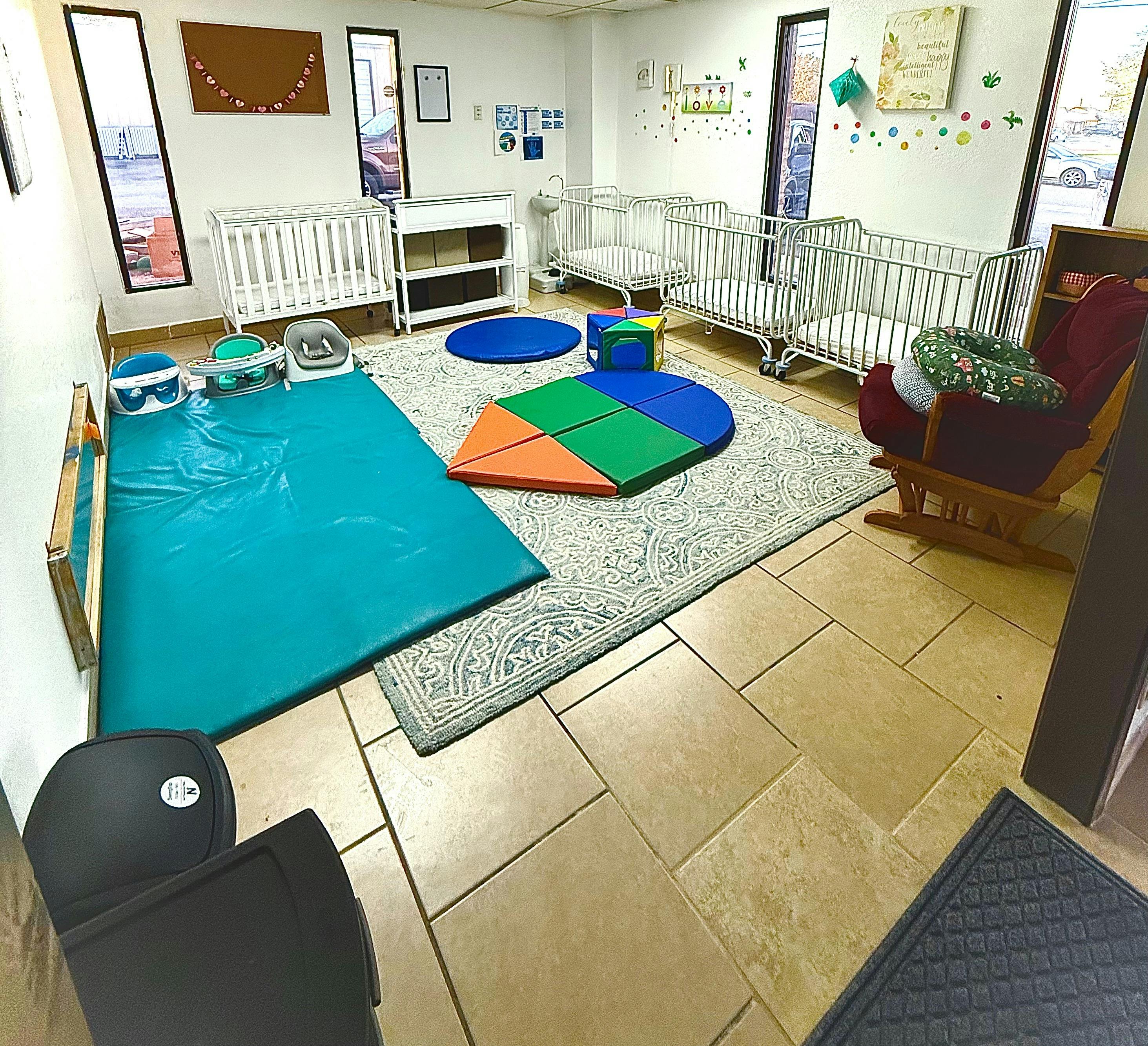 Nursery room with cribs, play mats, and a rocking chair