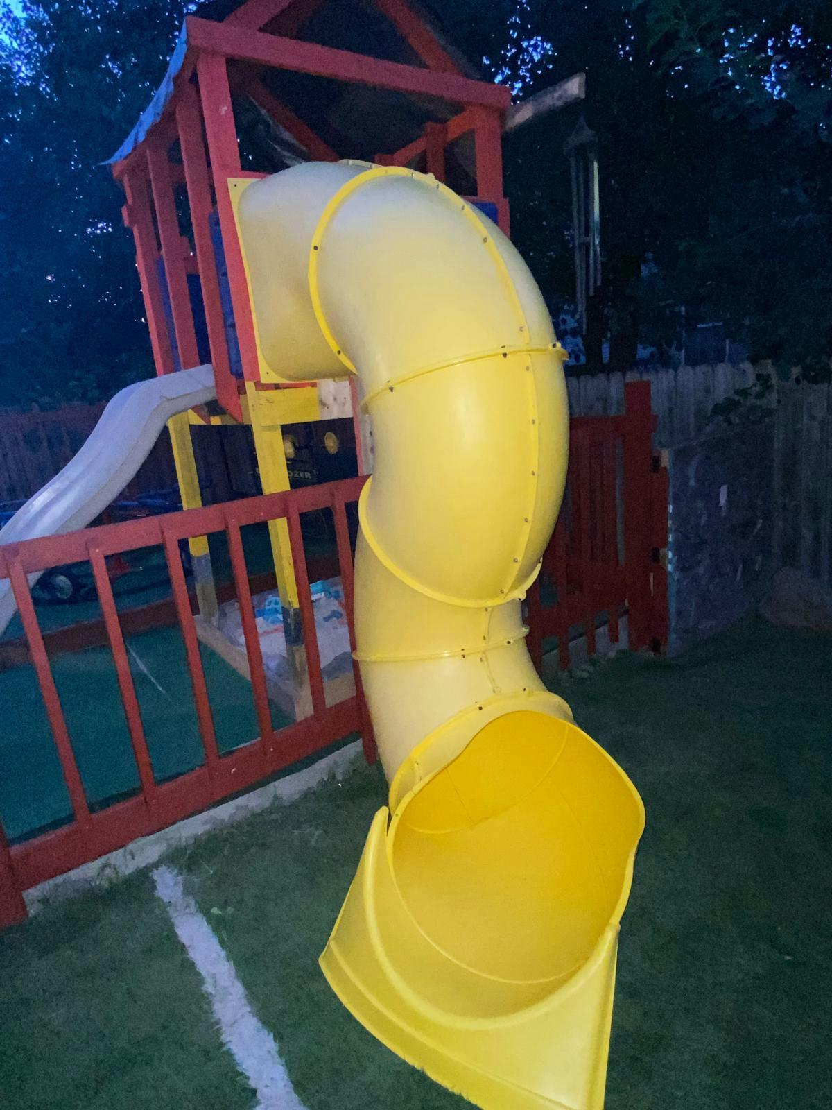 Yellow plastic tube slide attached to a wooden backyard play structure