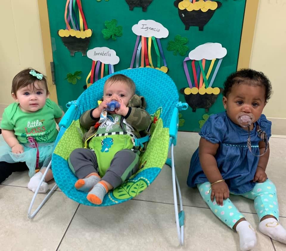 Three babies, one in a bouncer and two sitting on the floor