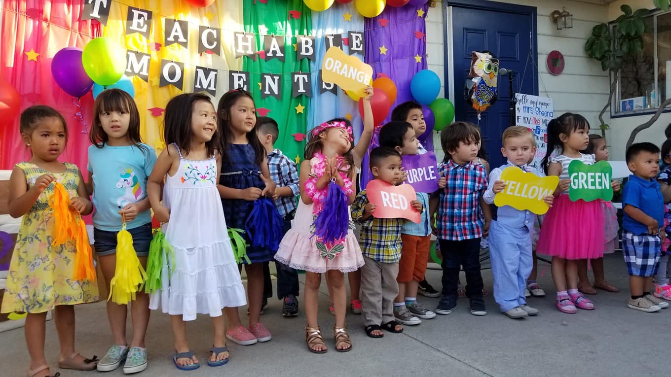 Group of children holding signs and pom-poms in front of a colorful banner