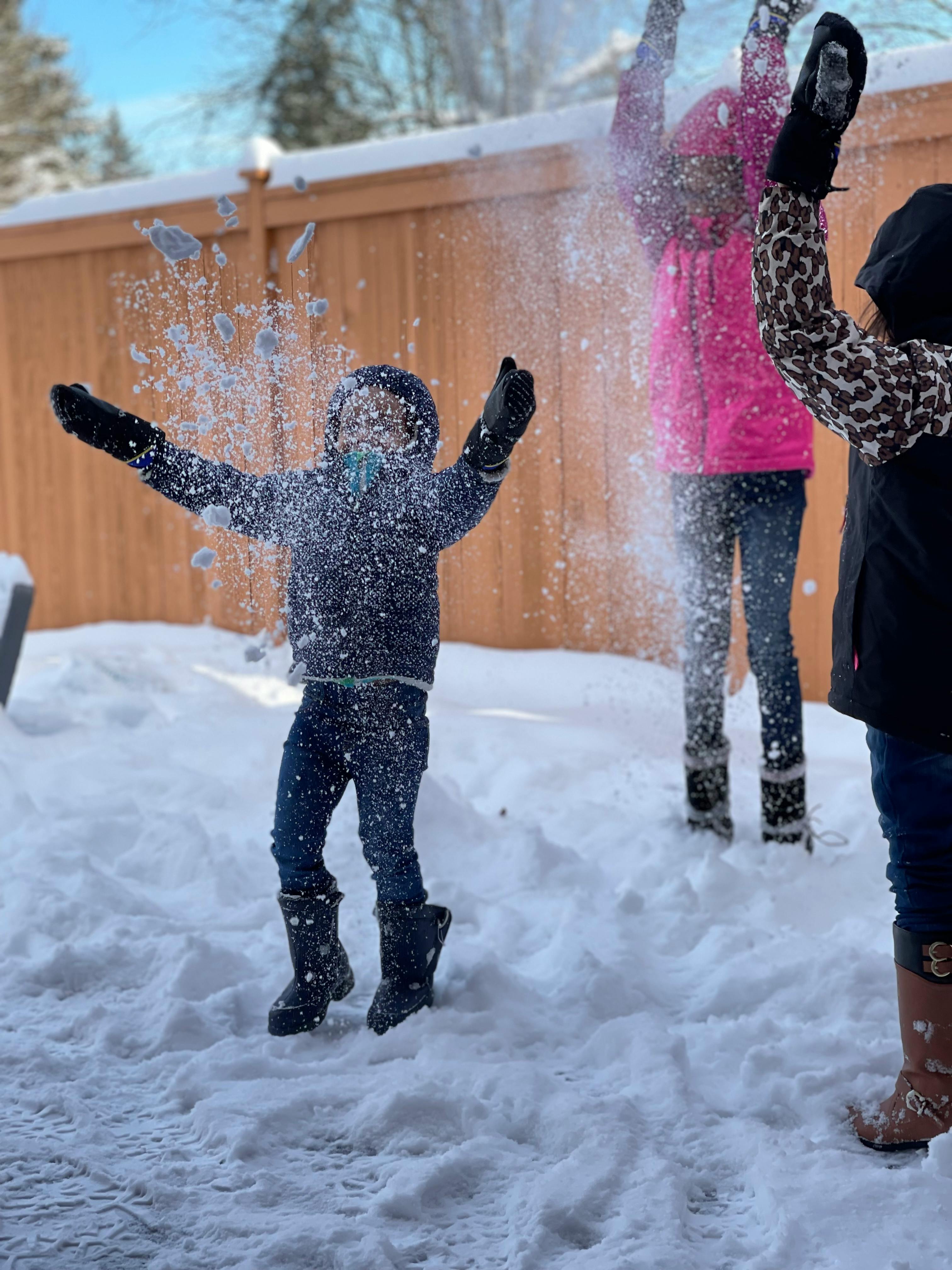 Child throwing snow in the air with other people in the background