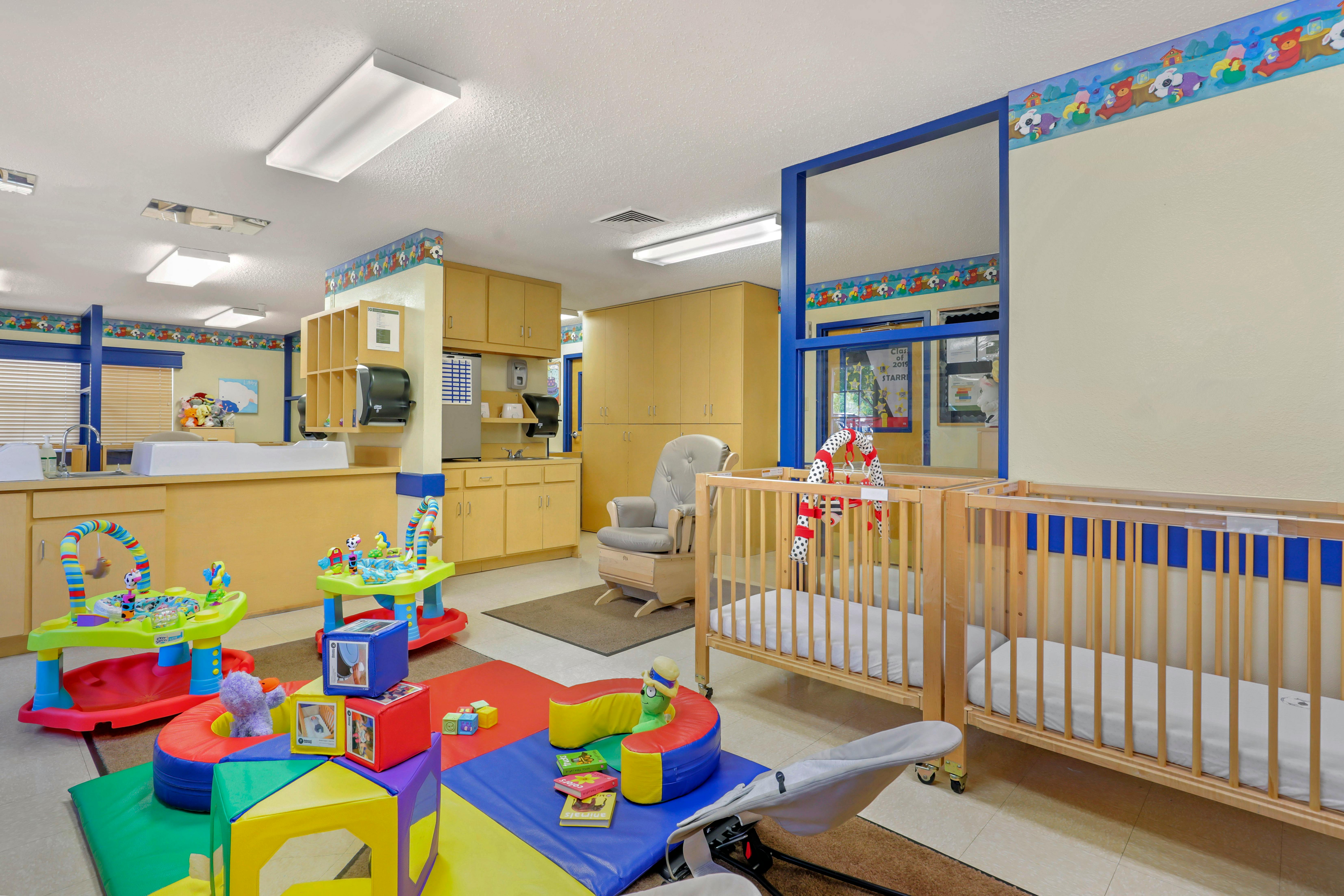 A colorful childcare room with cribs, play mats, and a changing station