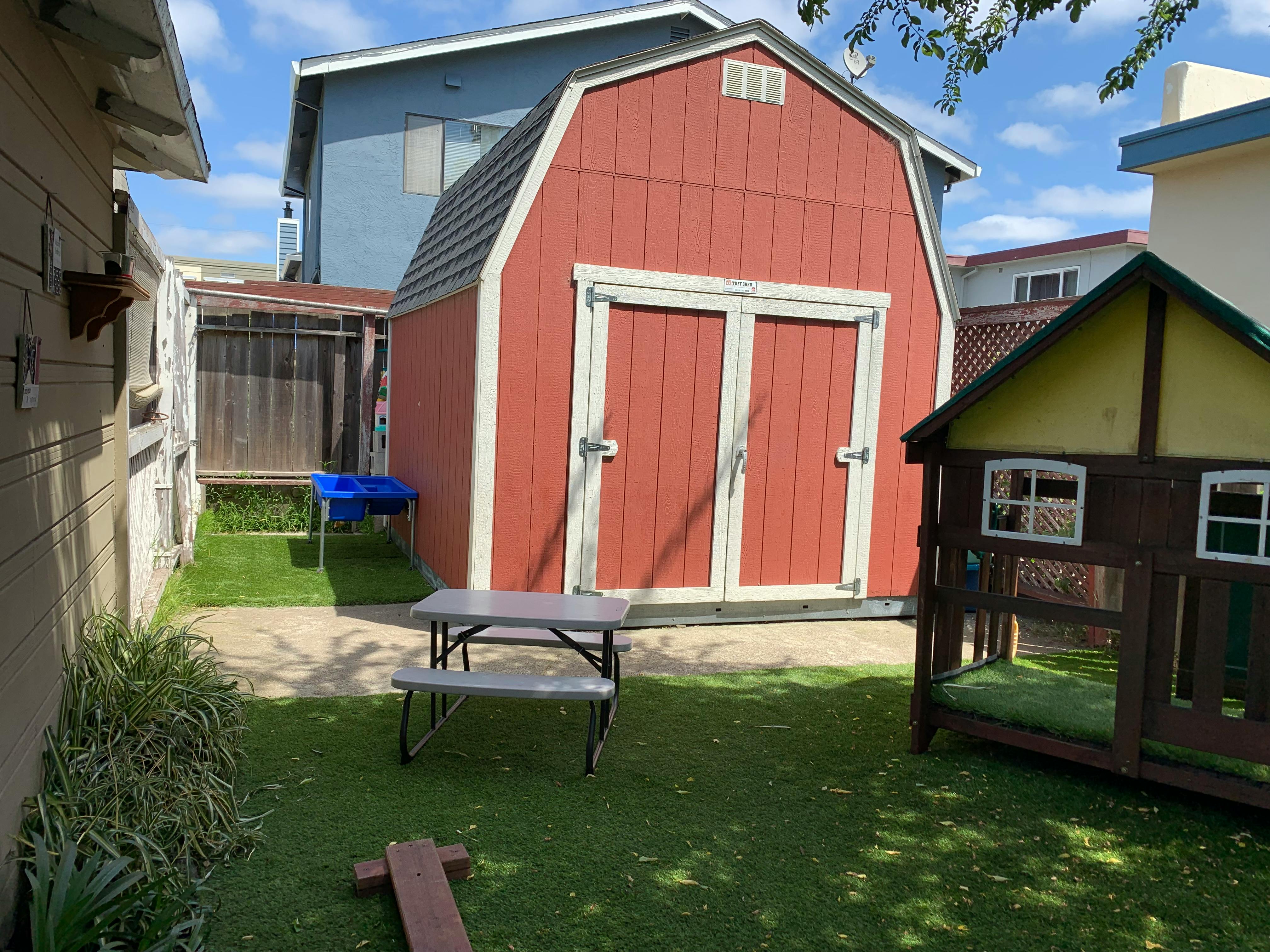 Red barn-style shed in a backyard with a small picnic table and playhouse