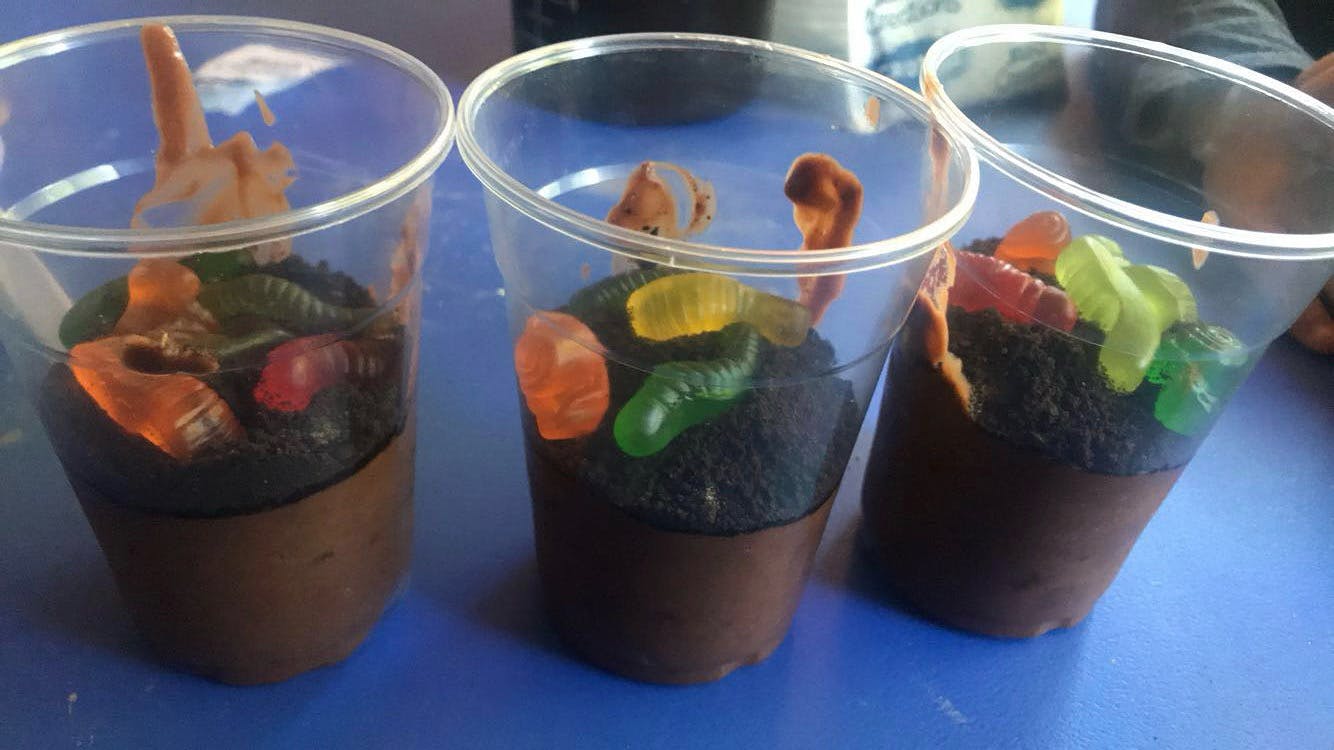 Three cups of chocolate pudding with crumbled cookies and gummy worms