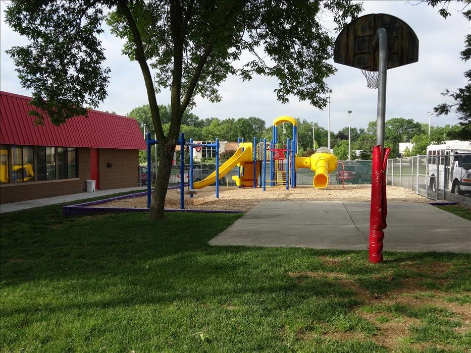 Playground with yellow slides and blue climbing structures, basketball hoop