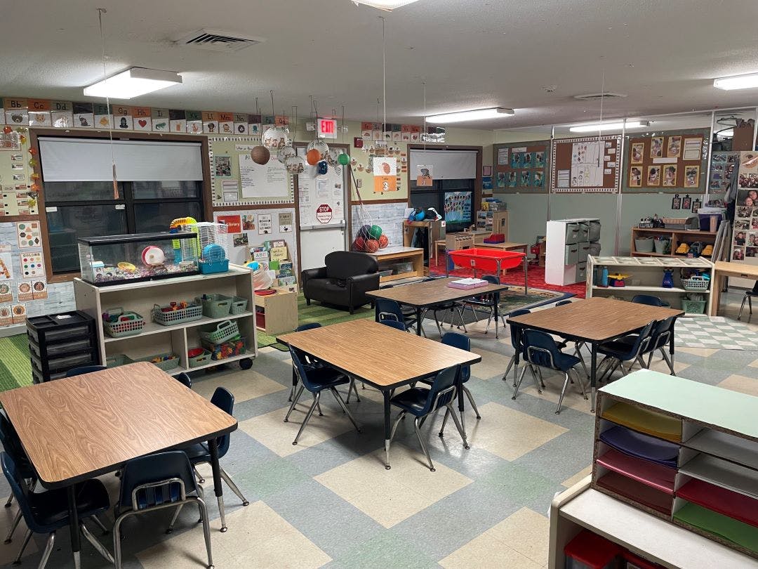 Empty classroom with small tables and chairs, a hamster cage, and learning decorations