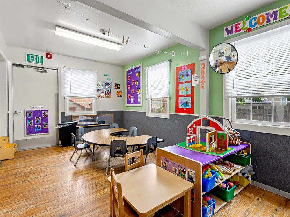 Classroom with tables, chairs, and shelves with toys and artwork on the walls