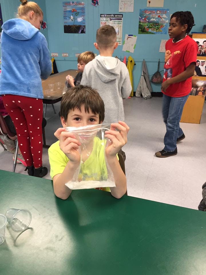 Child holding a plastic bag with white powder in a classroom