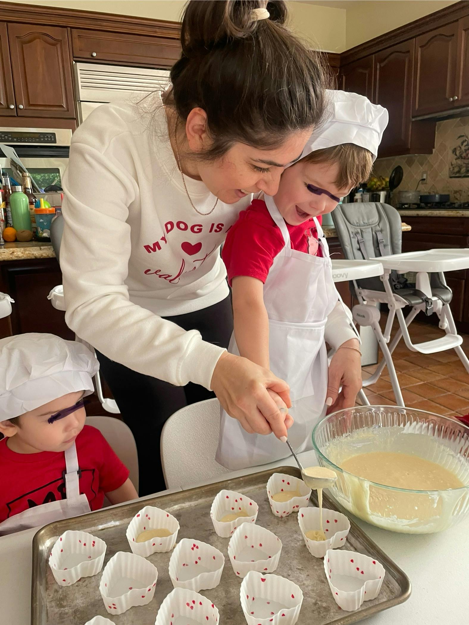 Person and child in chef hats and aprons pouring batter into cupcake liners