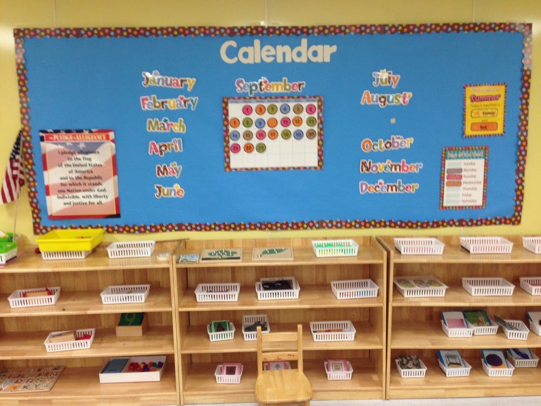 Classroom bulletin board with calendar and shelves with baskets