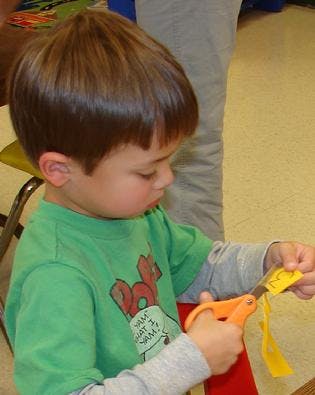 Child cutting yellow paper with orange scissors