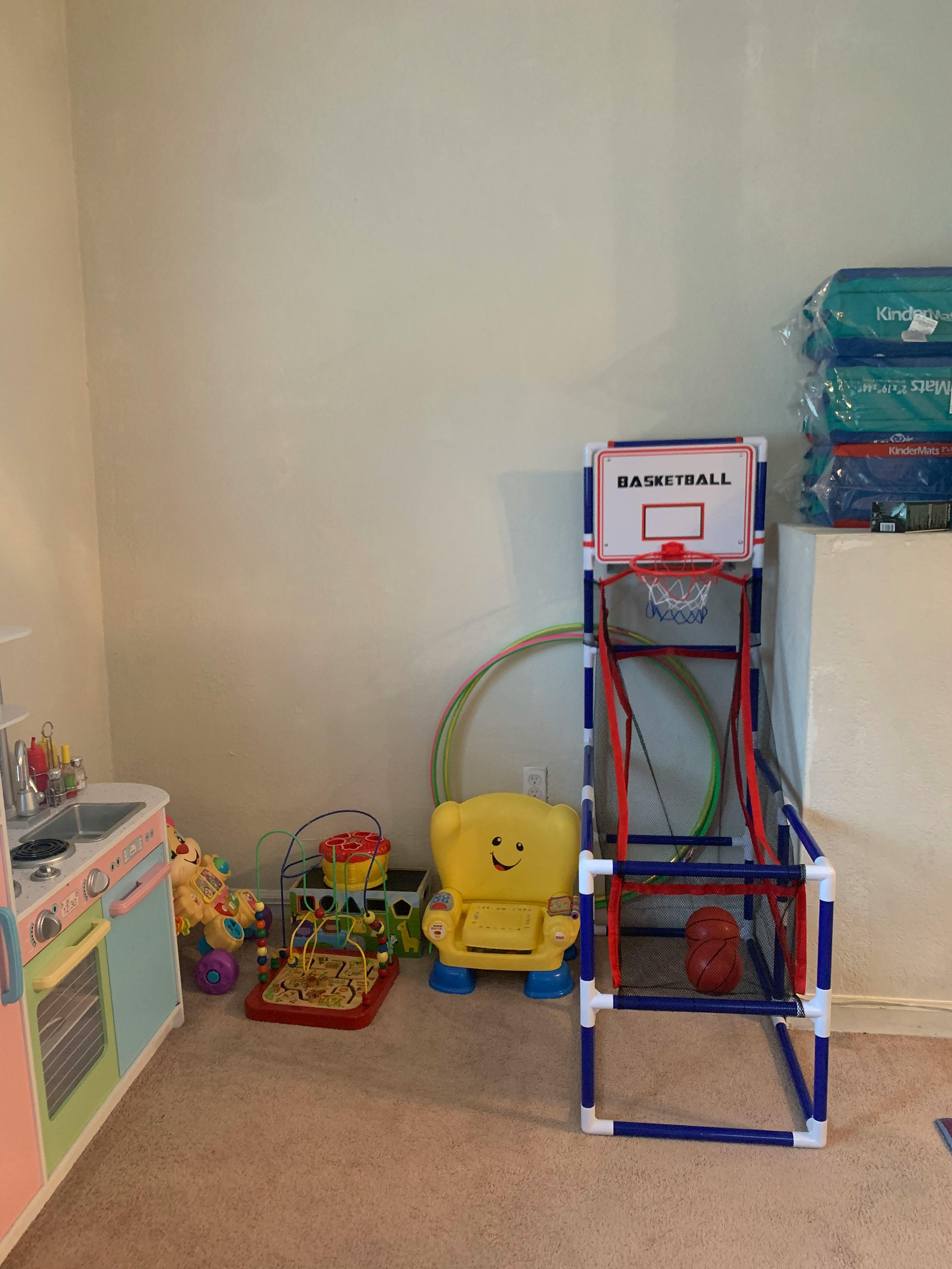 Children's play area with toy kitchen, basketball hoop, and yellow chair