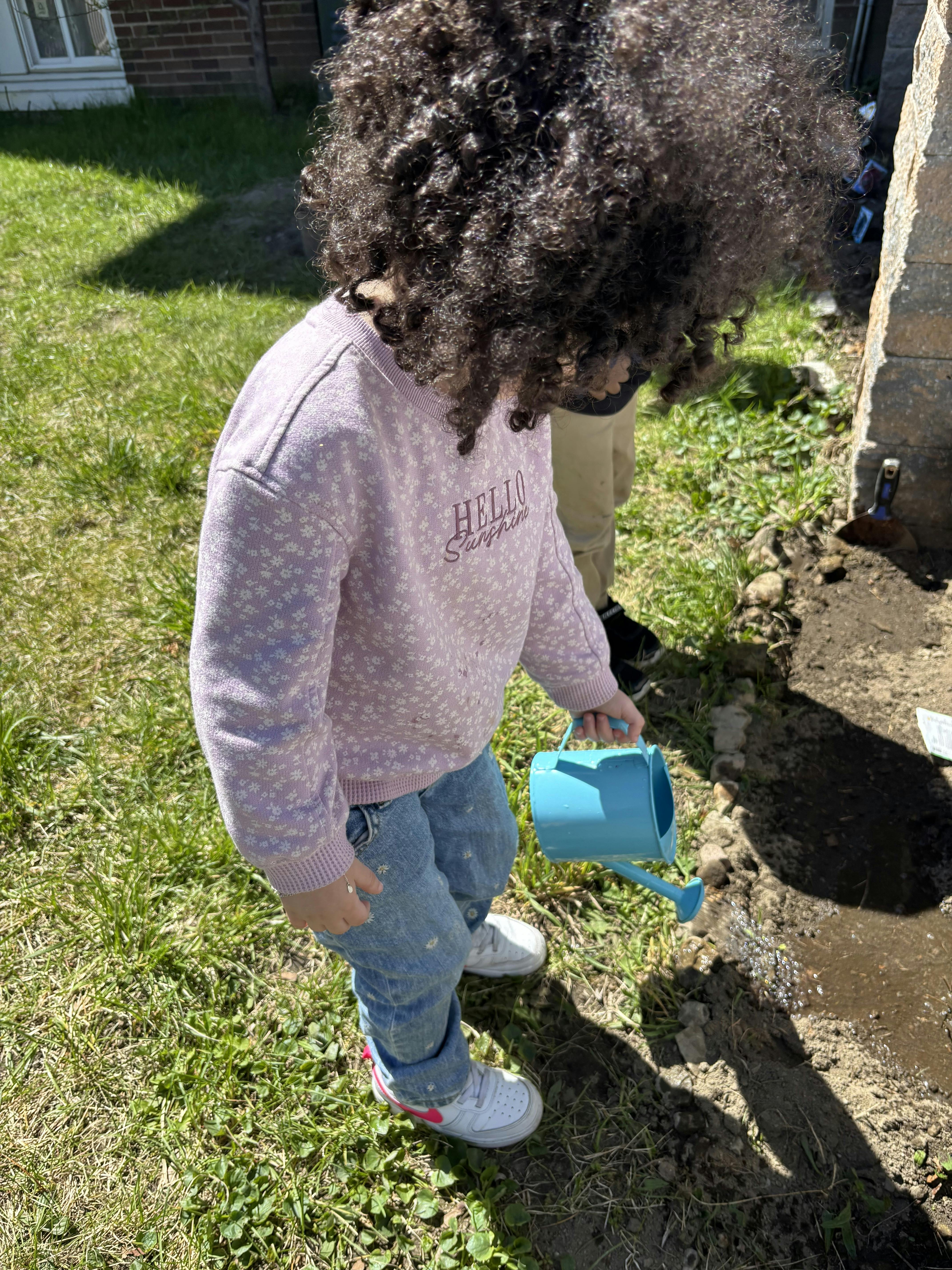 Child watering soil with a blue watering can
