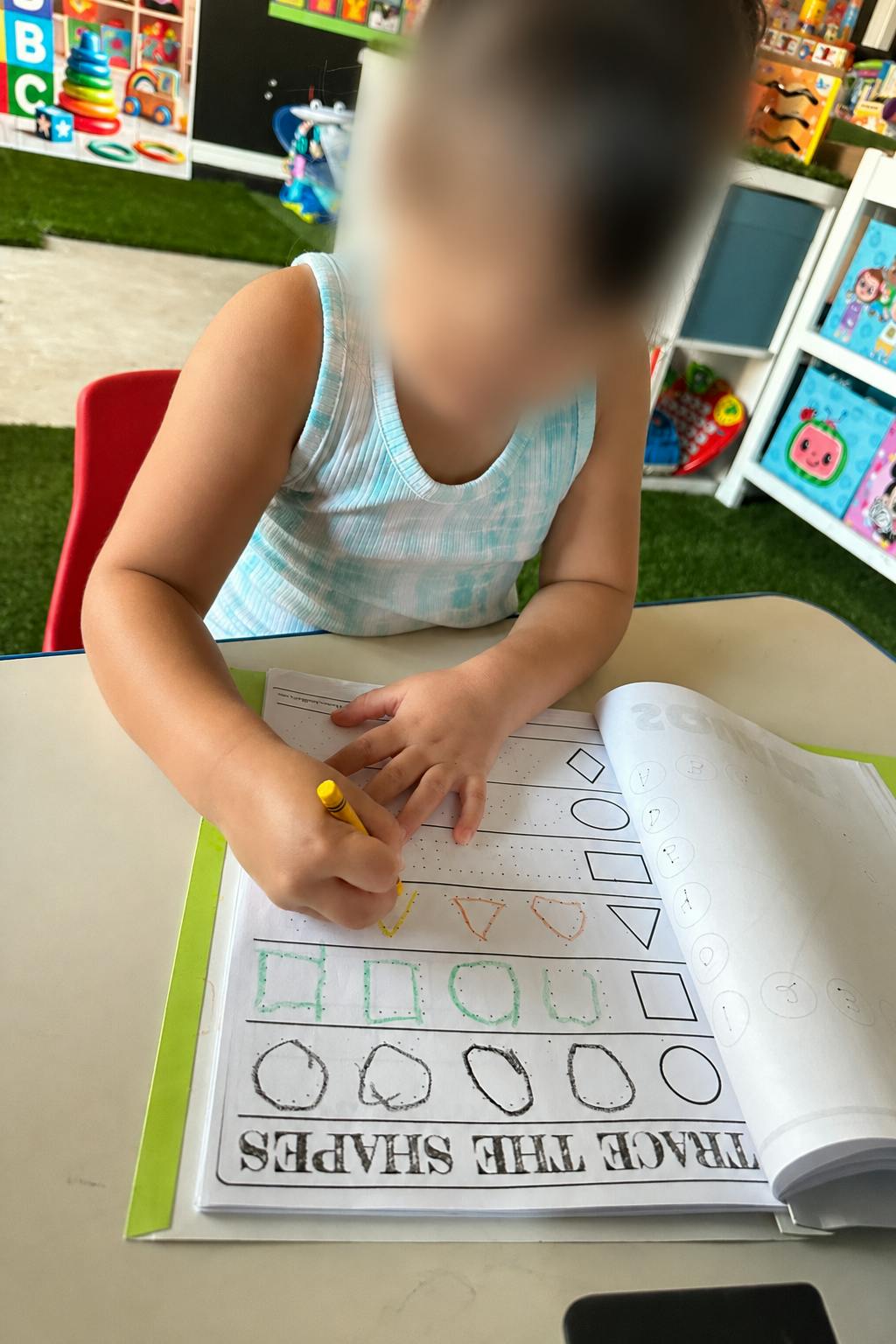 Child tracing shapes in a workbook at a desk