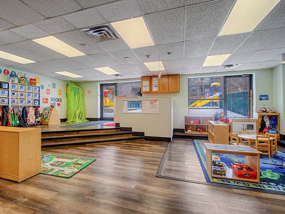 Colorful preschool classroom with tables, chairs, and playground visible through window