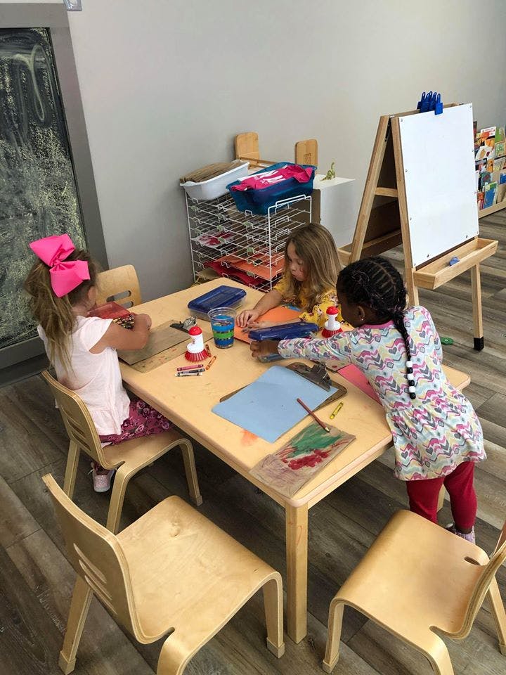 Three children drawing and coloring at a table in a classroom