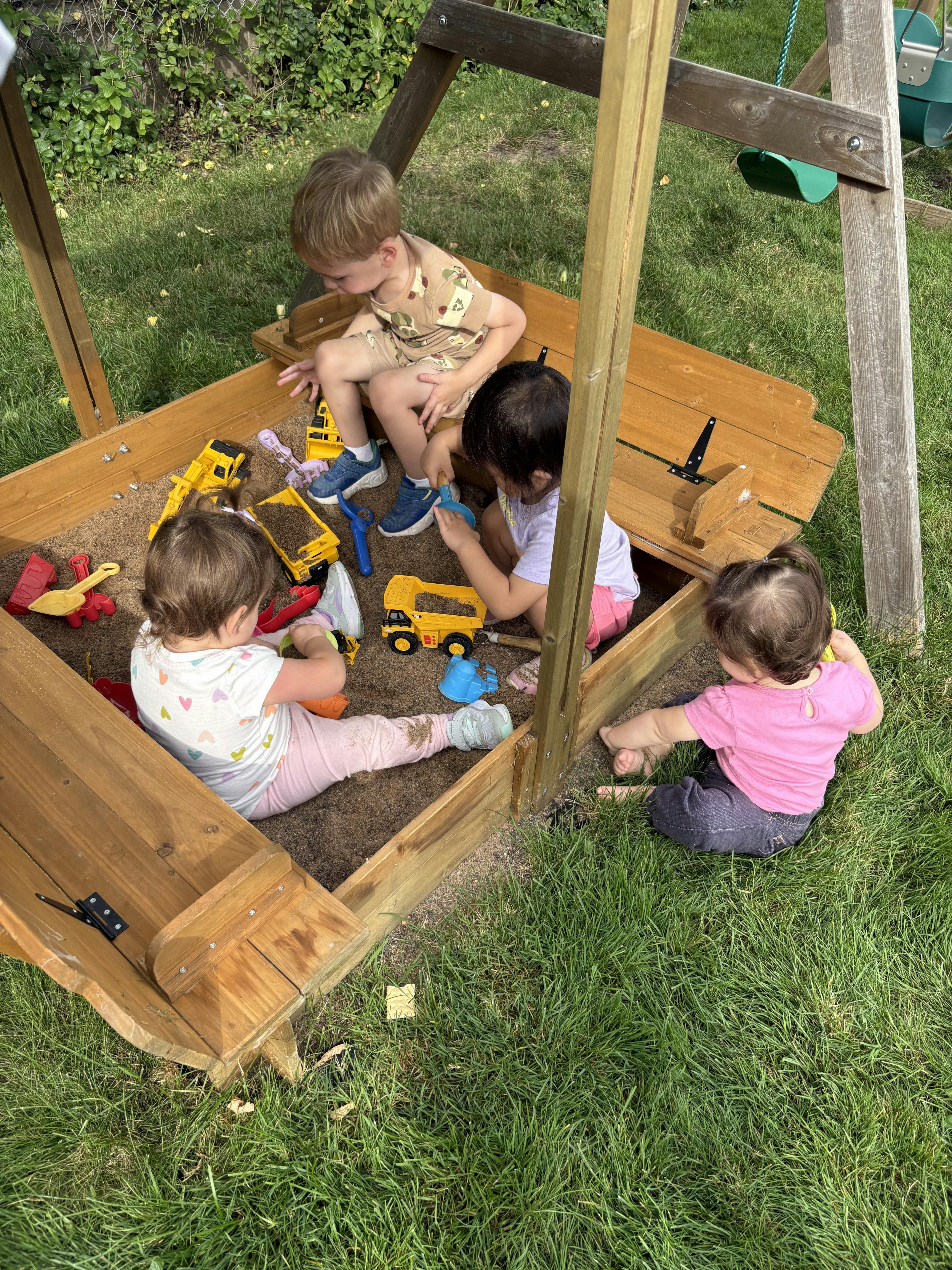 Children playing in a sandbox with toy trucks and shovels