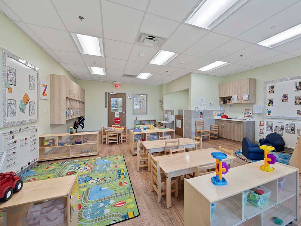 Classroom with child-sized tables and chairs, play rug, and storage shelves