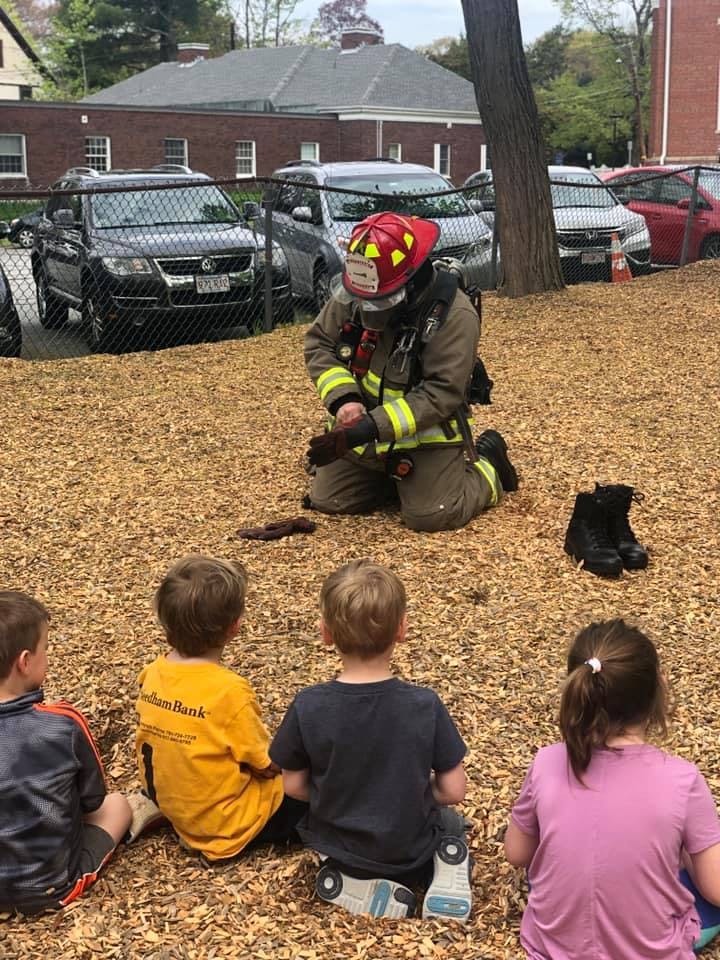 Firefighter kneeling in front of children on wood chips