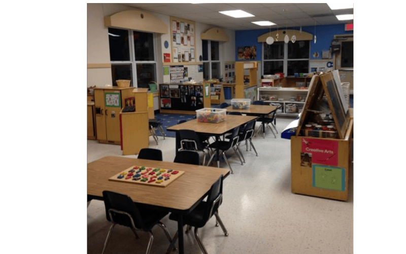 Empty preschool classroom with tables, chairs, and learning materials
