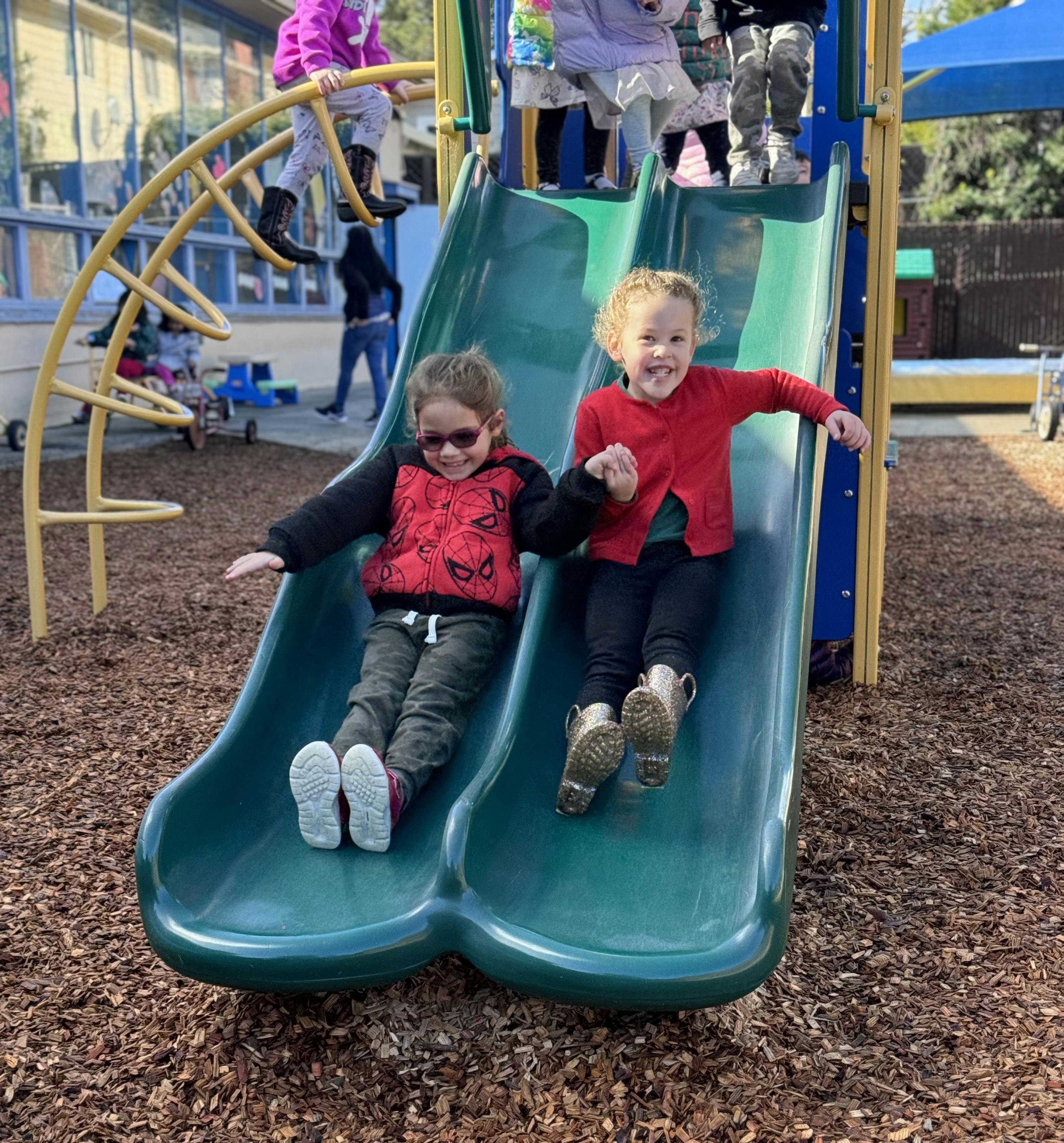 Two children sliding down a double slide on a playground