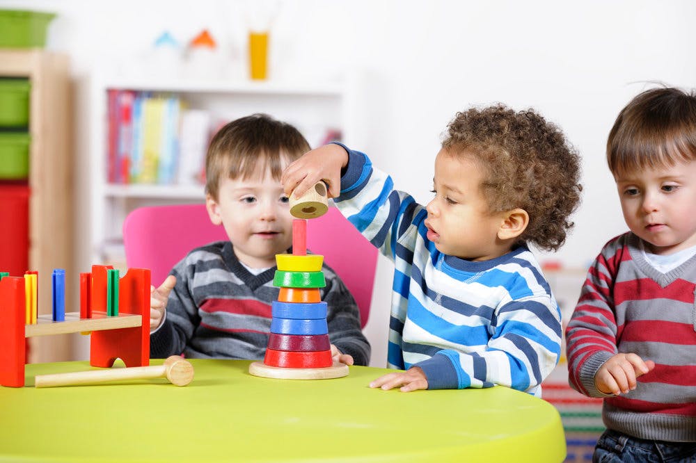 Three children playing with stacking toys and a wooden peg toy at a table