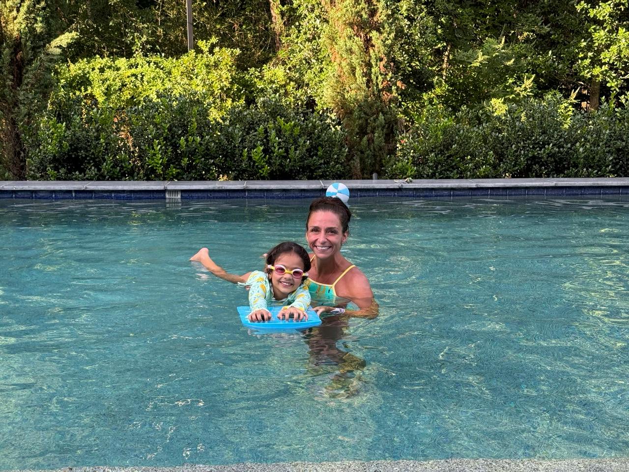 A person helping a child with a kickboard in a swimming pool