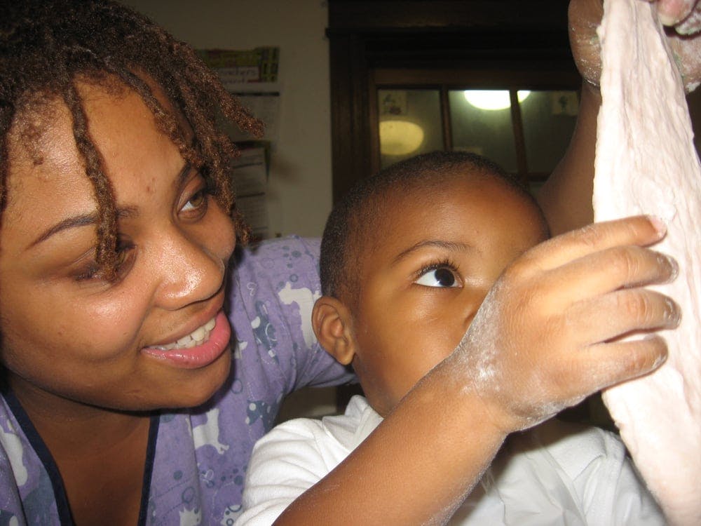 Person with dreadlocks looking at a child touching dough