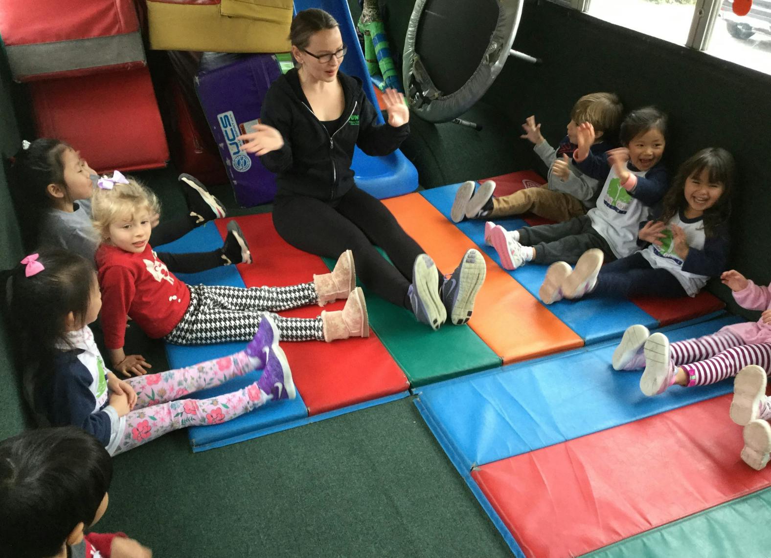 Adult and multiple children sitting on colorful mats