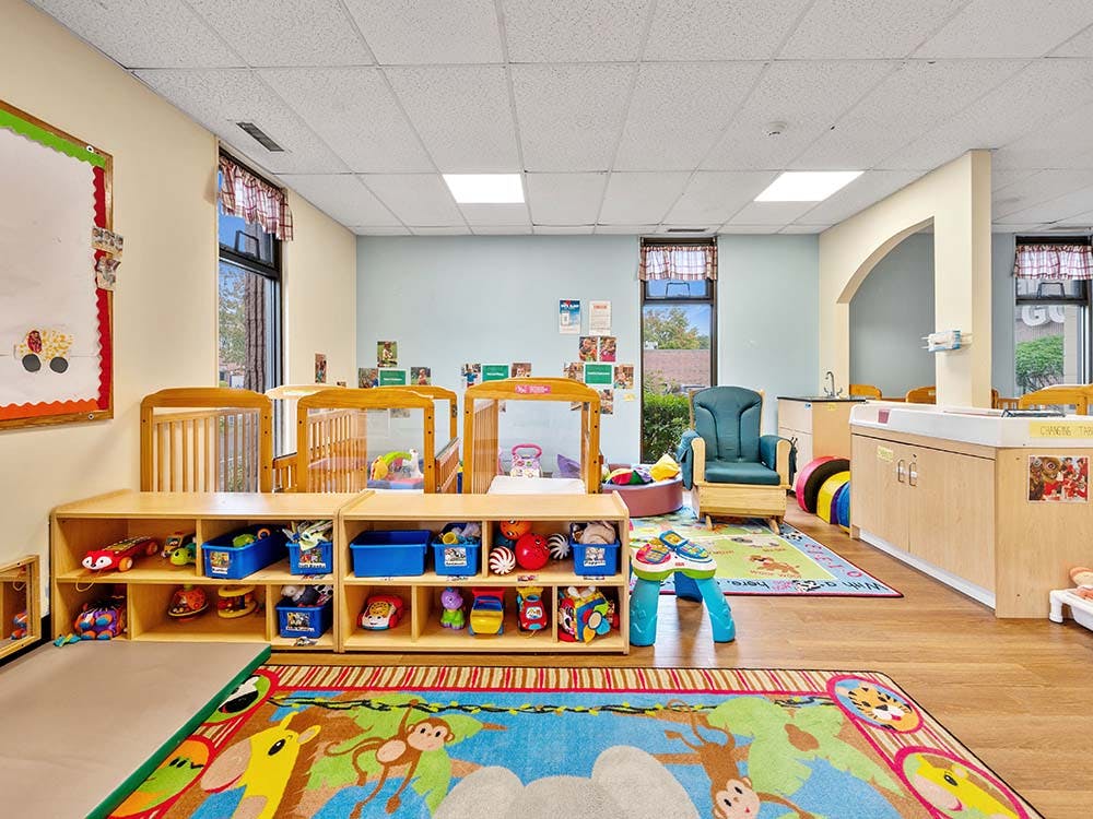 A colorful childcare classroom with cribs, shelves of toys, and a changing table