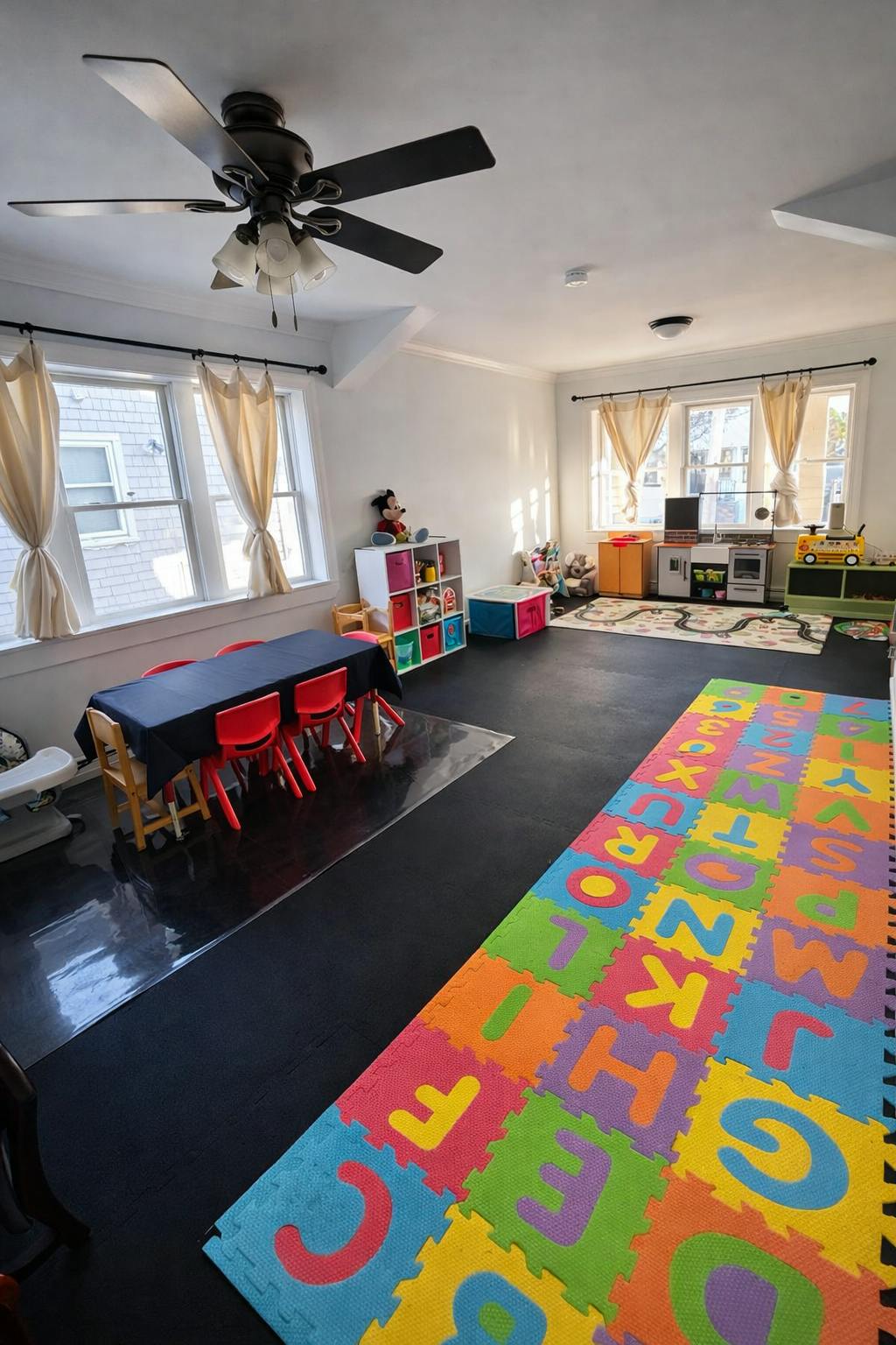 Playroom with a table, alphabet floor mats, and toy furniture