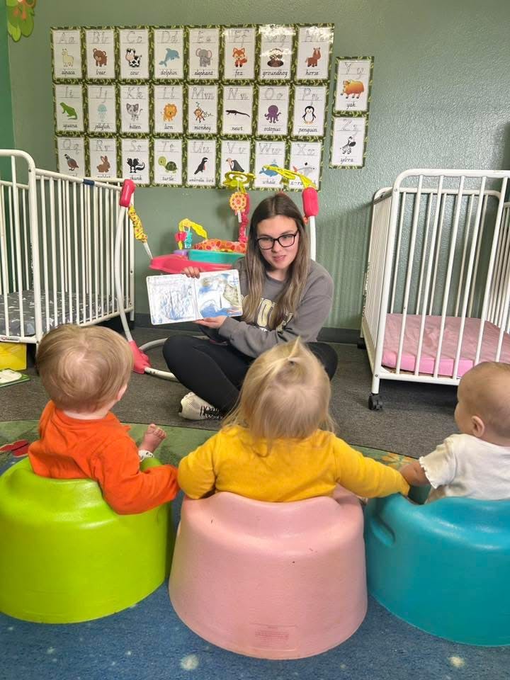 Person reading a book to three children in a classroom