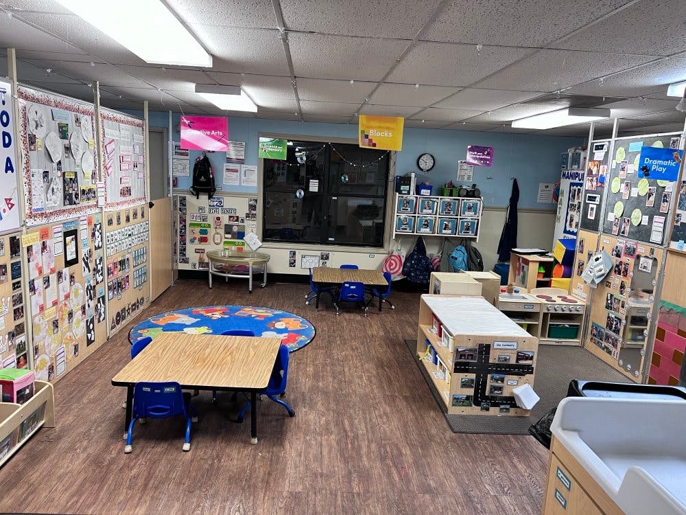 An empty classroom with small tables and chairs, activity centers, and display boards