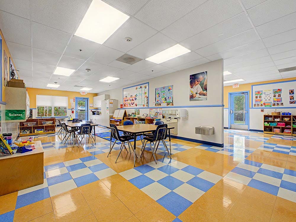 Empty classroom with checkered floor, small tables, chairs, and learning materials