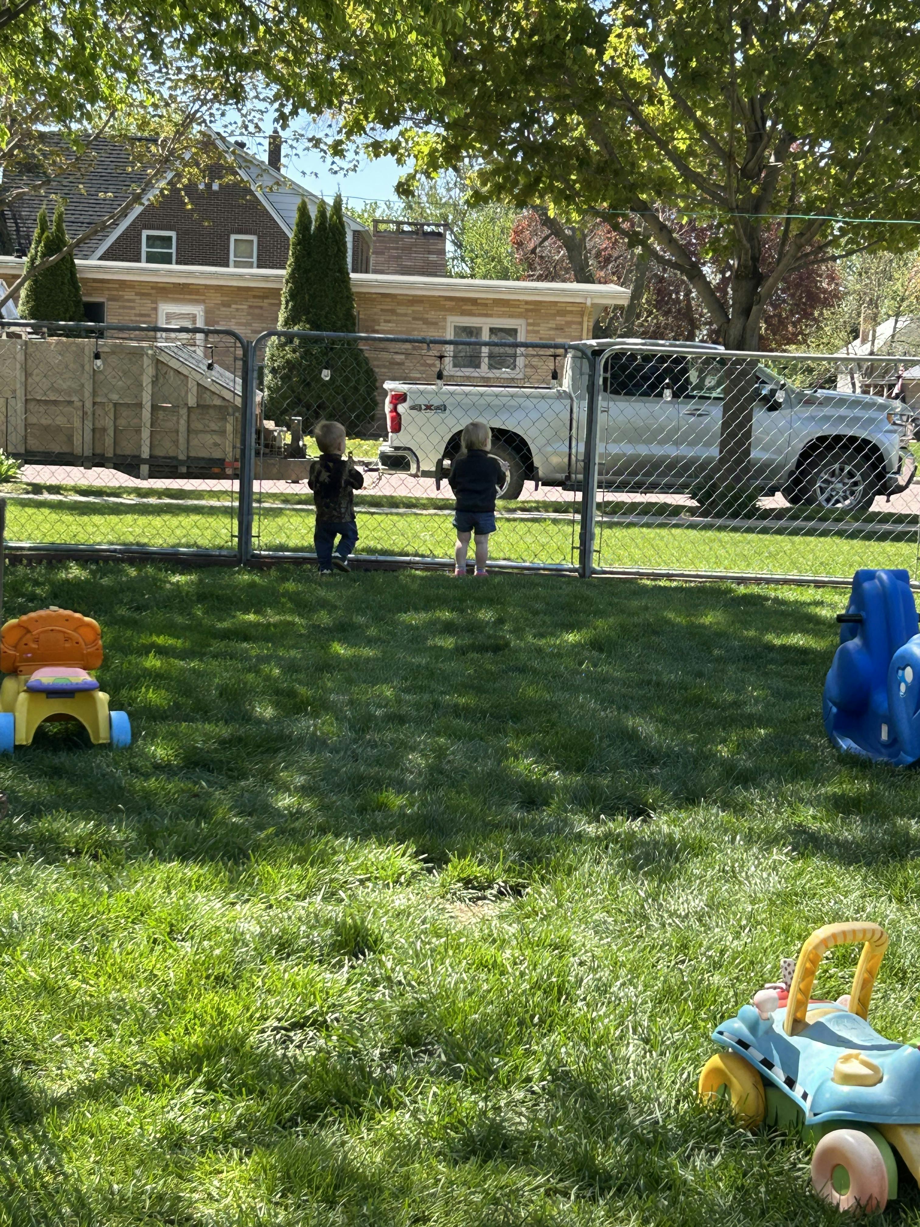 Two children standing at a fence, looking out into a residential area