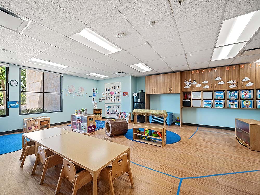 Children's classroom with wooden tables and chairs, play kitchen, and storage