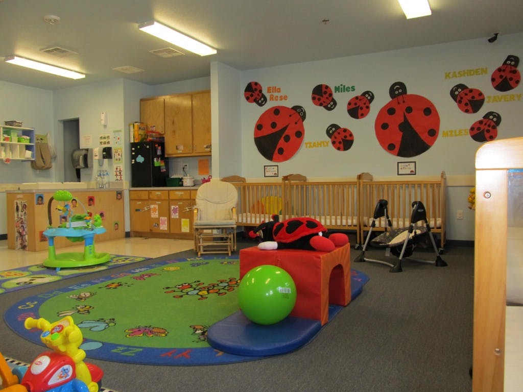 Daycare room with cribs, play mat, and ladybug wall decals