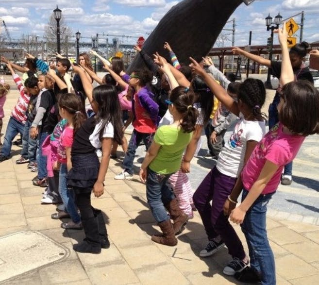 Children pointing up at a large dark sculpture