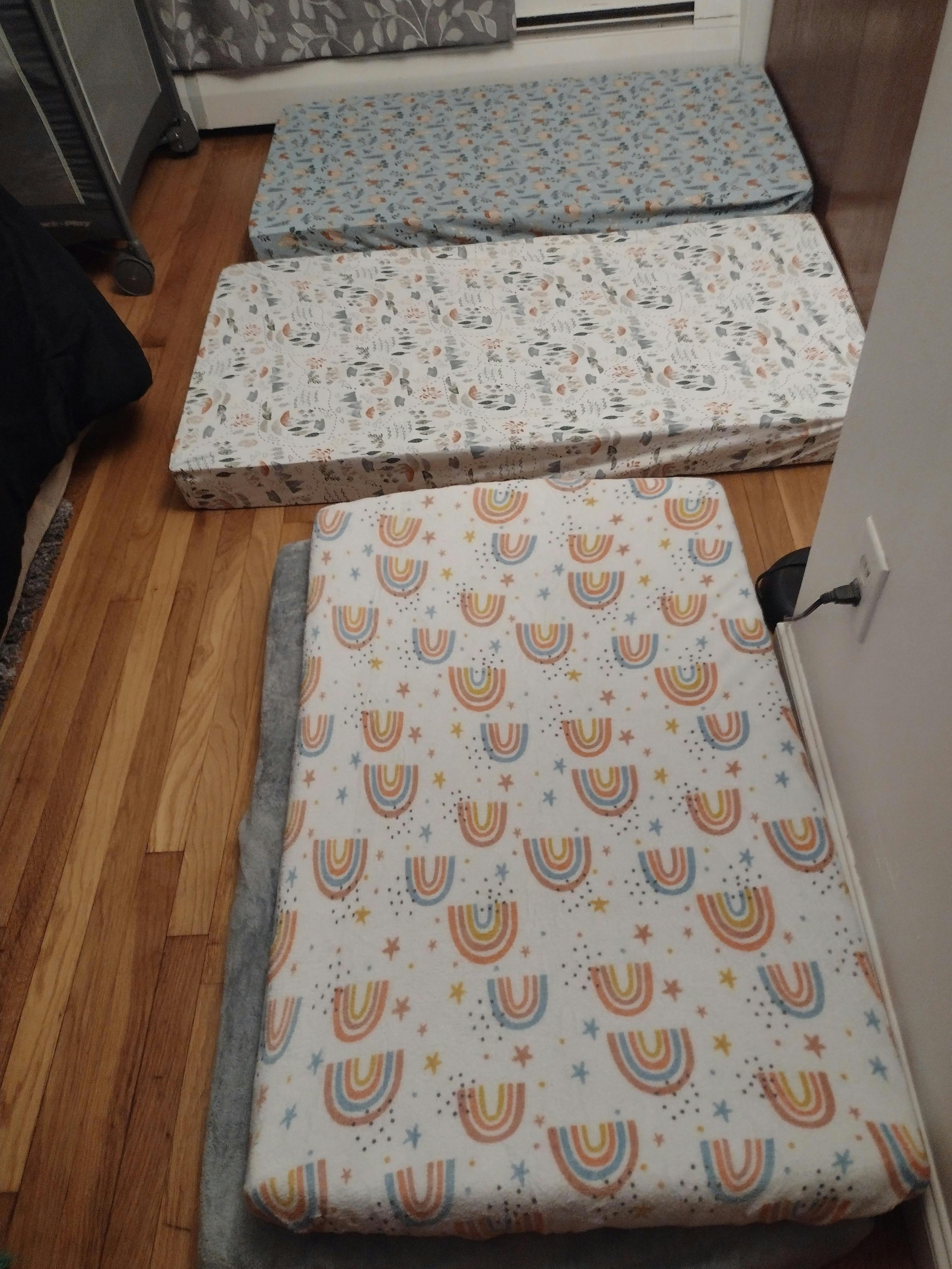 Three mattresses with patterned sheets on a wooden floor