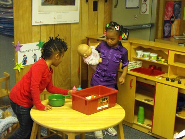 Two children playing with a doll and toys in a classroom
